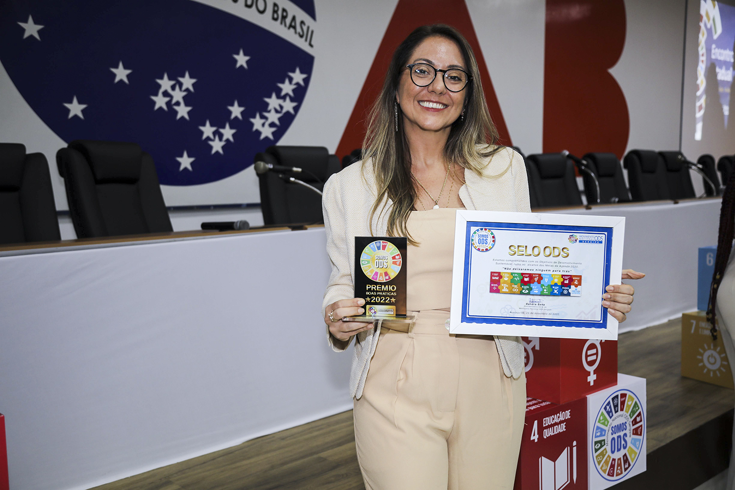 Karyna Sposato, coordenadora dos Observatórios Sociais da UFS, exibe quadro com Selo ODS e troféu do Prêmio boas práticas ODS 2022